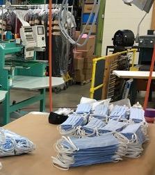 In the foreground, non-surgical face masks being produced by Jostens in facilities originally designed for graduation products (in the background). 