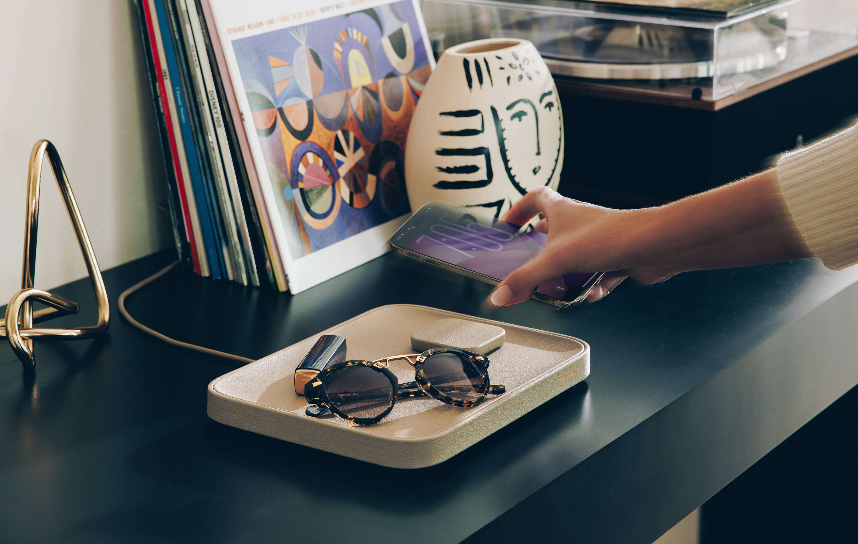 Twelve South Valet in Taupe leather organizing sunglasses and charging an iPhone on a modern console table with vinyl records in the background.