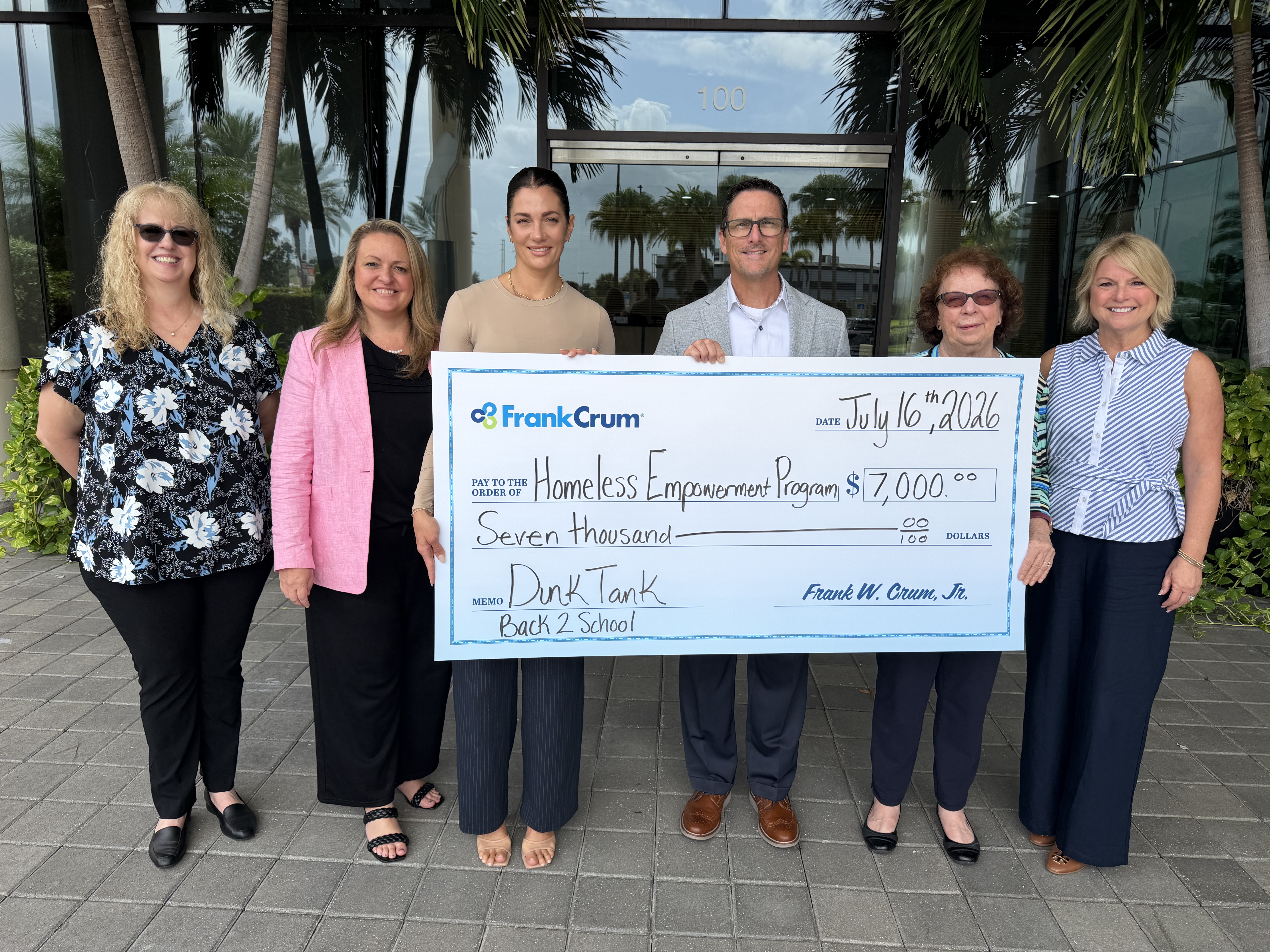 FrankCrum representatives present a ceremonial check to the Homeless Empowerment Program outside the FrankCrum company building.