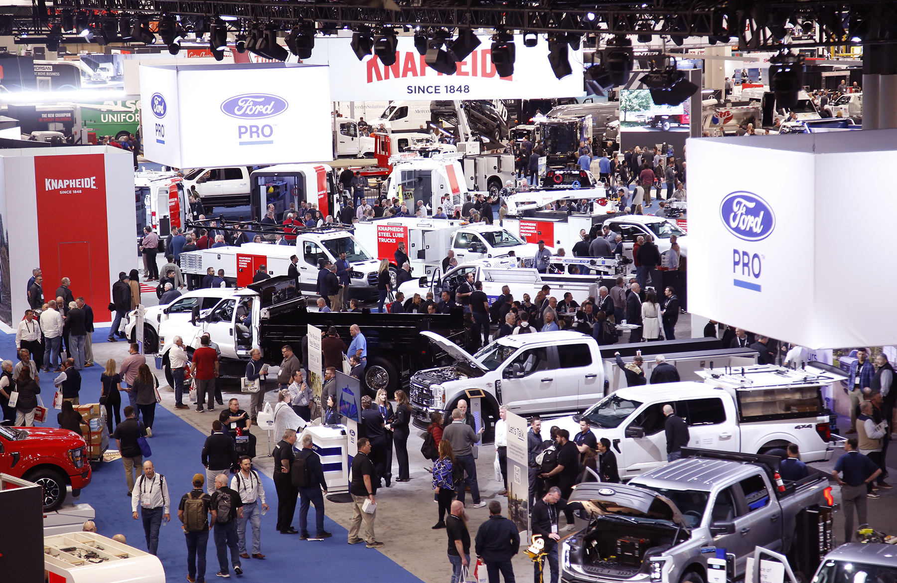 People walk through Work Truck Show exhibit hall full of work trucks, vans and other commercial vehicles