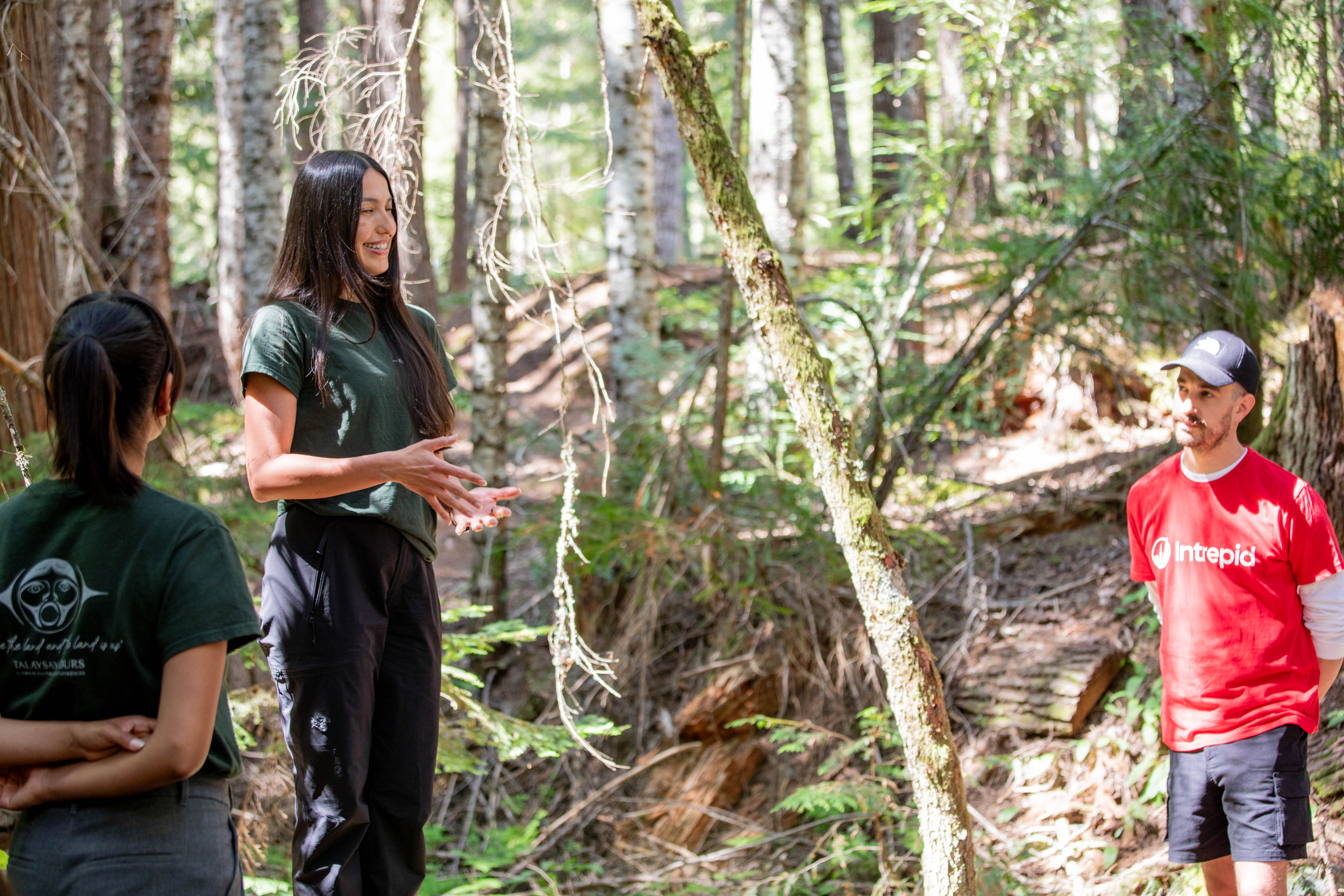 A Talaysay Tours guide leads an Indigenous-led experience in a forest in Whistler, B.C., with an Intrepid Travel representative looking on.