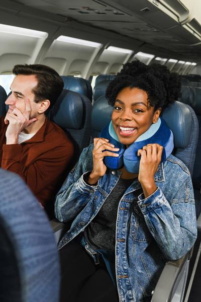 Image shows a woman wearing a Cabeau Evolution Earth neck pillow on an airplane