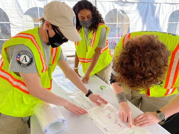 A team of AmeriCorps members serving with the National Civilian Community Corps creates signage to be used within a vaccination center at the Miami-Dade Community College North Campus.   